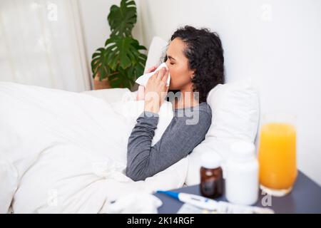 Une jeune femme multi-ethnique lui souffle le nez tout en se rétablissant de la grippe au lit Banque D'Images