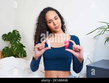 Une jeune femme multi-ethnique tient le tampon et la coupe menstruelle pour le choix de comparaison Banque D'Images