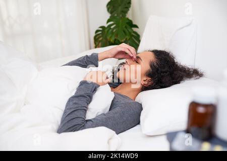 Une jeune femme multiethnique tient son nez dans la douleur couchée au lit de la migraine Banque D'Images