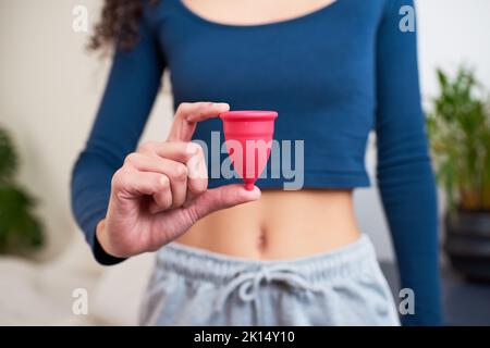 Gros plan d'une jeune femme tenant une coupe menstruelle en pyjama Banque D'Images