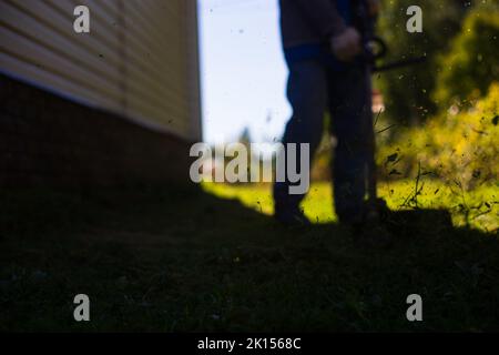 Homme fauchant de l'herbe haute à l'aide d'un coupe-herbe électrique ou à essence dans l'arrière-cour. Outils et équipements de jardinage. Processus de tonte de la pelouse avec la tondeuse à main Banque D'Images
