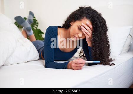 Une jeune femme multi-ethnique se couche au lit en regardant les résultats indésirables des tests de grossesse Banque D'Images