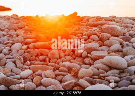 Pierres et galets sur la plage de Trefor, au nord du pays de Galles, avec un coucher de soleil rouge orangé Banque D'Images