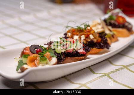 Bruschetta avec diverses garnitures, une variété de petits sandwiches sur une assiette blanche. Banque D'Images