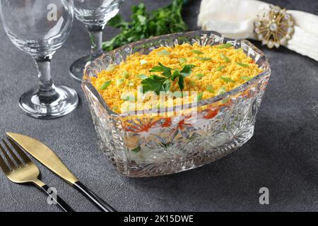 Couches de salade de fête Mimosa avec poisson en conserve, pommes de terre, fromage, carottes et œufs dans un saladier transparent sur fond gris Banque D'Images