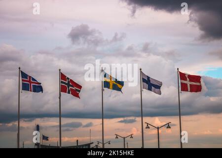 Les drapeaux des pays scandinaves contre un ciel nuageux au coucher du soleil. Banque D'Images