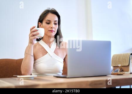 Femme indépendante concentrée avec une tasse de café regardant l'écran de netbook tout en travaillant sur le projet à distance dans le café Banque D'Images