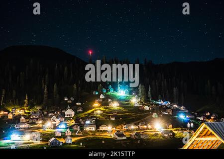 Maisons de village avec éclairage lumineux situé près des arbres de forêt sur la pente de la montagne à la nuit sombre Banque D'Images