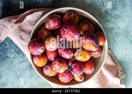 Fruits de prune frais biologiques et mûrs dans le bol sur fond de béton Banque D'Images