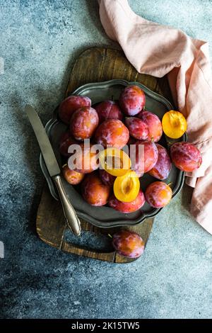 Fruits de prune frais biologiques et mûrs dans une assiette sur fond de béton Banque D'Images