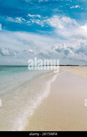 Vagues transparentes d'eau de mer propre roulant sur la plage de sable de l'île de Thulusdhoo contre ciel bleu nuageux aux Maldives Banque D'Images