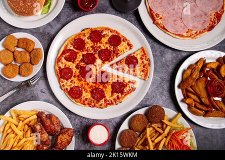 Vue de dessus de l'assiette avec une délicieuse pizza au pepperoni et un bol de sauce avec des plats de junk variés placés sur une table grise pendant le déjeuner Banque D'Images