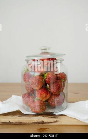 Fraises entières fraîches et crues dans un pot en verre placé sur une planche à découper en bois sur une table dans la cuisine Banque D'Images