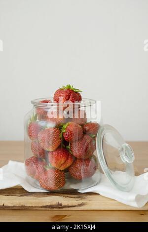 Fraises entières fraîches et crues dans un pot en verre placé sur une planche à découper en bois sur une table dans la cuisine Banque D'Images