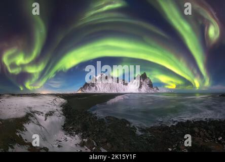 Vue à couper le souffle sur l'eau calme et la montagne enneigée de Vestrahorn et le ciel nocturne avec aurore verte en hiver en Islande Banque D'Images