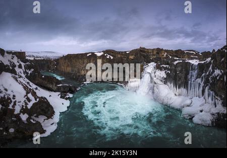 Vue pittoresque de drone de la cascade d'Aldeyjarfoss tombant d'une falaise de neige rugueuse contre ciel nuageux en soirée en hiver en Islande Banque D'Images