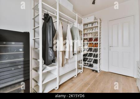 Garde-robe avec divers vêtements colorés et élégants accrochés sur des étagères avec des vêtements pliés près de la porte en verre dans l'appartement lumineux Banque D'Images