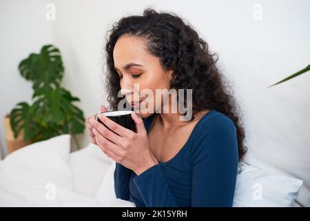 Une jeune femme multi-ethnique souffle sur son café pour le refroidir se réveillant au lit Banque D'Images