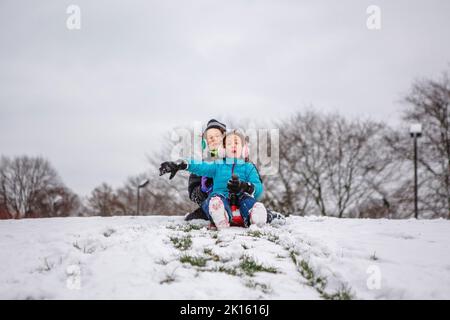 Deux enfants glissent ensemble sur une colline enneigée en hiver Banque D'Images