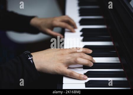 Gros plan sur les mains de la femme jouant du piano en lisant de la musique en feuilles. Ambiance sombre. Banque D'Images