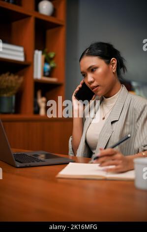 Portrait, femme d'affaires asiatique attirante et professionnelle du millénaire à son bureau, traitant ses affaires au téléphone avec son fournisseur. Banque D'Images