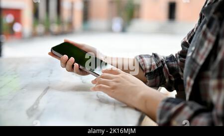 Une femme utilise son smartphone pour discuter avec ses amis en étant assise à l'extérieur du bâtiment. Gros plan et image de vue arrière. Banque D'Images