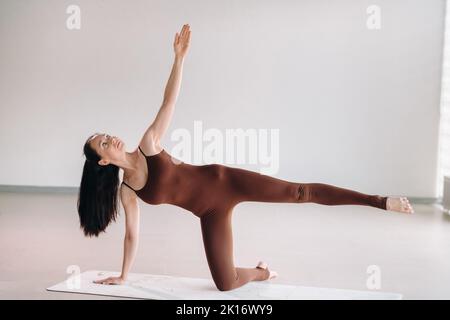 une femme en costume marron fait du yoga dans une salle de fitness. Mode de vie sain, forme physique, entraînement, autosoins Banque D'Images