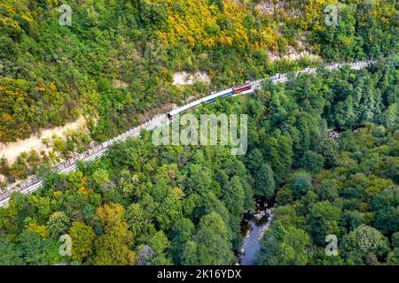 Le train traverse une montagne près de la rivière, tir de drone aérien. Banque D'Images
