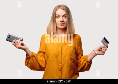 Services bancaires mobiles. Client féminin confus. Problème de transaction. Vérification des données personnelles. Femme troublée avec peur dans un chemisier orange avec téléphone à carte de crédit Banque D'Images