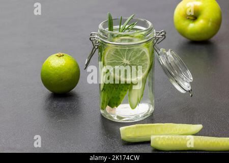 Boisson d'été avec citron vert et concombre dans un pot. Tranches de concombre sur la table. Citron vert et pomme sur table. Arrière-plan noir. Banque D'Images