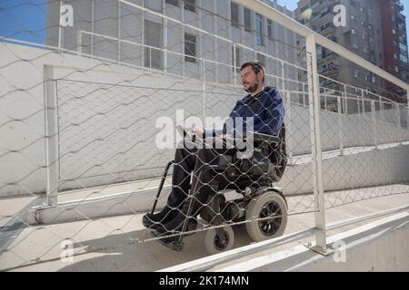 Homme en fauteuil roulant, approchant le bâtiment le long d'une rampe accessible pour les personnes handicapées Banque D'Images