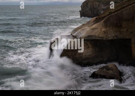 Vagues éclaboussant sur des rochers à tunnel Beach, Dunedin. Photo prise à une vitesse d'obturation lente montrant le mouvement des vagues. Banque D'Images