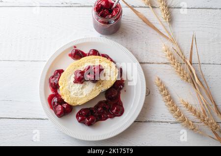 Dessert à la cerise avec compote de cerise aigre et rouleau suisse rempli de crème fouettée sur fond blanc Banque D'Images