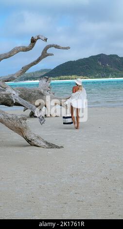 Femme dans un chapeau de seau et une chemise blanche tenant un sac fourre-tout marchant à côté du célèbre arbre sur la plage de Whitehaven dans les Whitsundays, en Australie. Banque D'Images