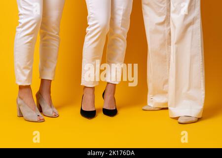 Style de vie des femmes. Confiance en la puissance. Succès de la richesse. Trois jambes de femme en pantalon blanc gris noir élégant chaussures debout ensemble isolé sur jaune vif Banque D'Images