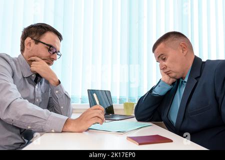 Jeunes hommes et jeunes cadres dirigeants qui communiquent avec un partenaire ou un client. Concentré deux hommes d'affaires assis à la table, impliqués dans un sérieux nego Banque D'Images