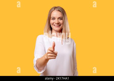 Bon travail. Geste encourageant. Femme de soutien. Salutation réussie. Portrait de dame gaie en blanc pointant vers l'appareil photo souriant isolé sur l'ém orange Banque D'Images