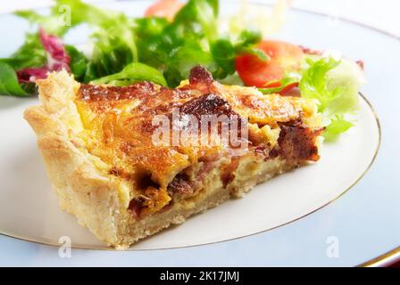 Une tranche de bacon et une quiche au fromage lorraine sur une assiette bleue avec une vinaigrette à la salade feuillue Banque D'Images