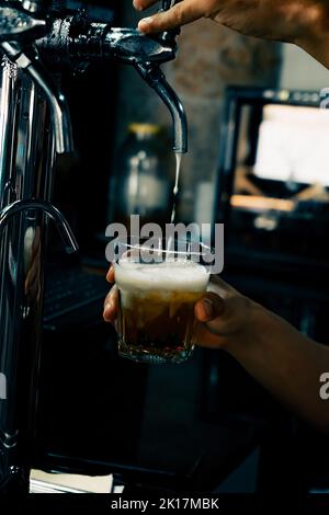 Servir la bière à la main dans le verre à l'aide du robinet. Le barman verse de la bière tout en se tenant au comptoir du bar. Main de Barman à la bière pression verser une bière pression. Banque D'Images