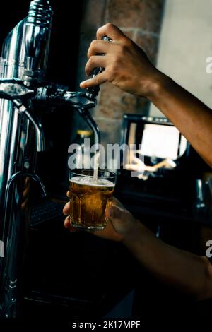 Servir la bière à la main dans le verre à l'aide du robinet. Le barman verse de la bière tout en se tenant au comptoir du bar. Main de Barman à la bière pression verser une bière pression. Banque D'Images