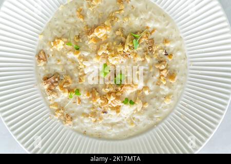 Risotto délicieux et crémeux, accompagné de fromage et de noix sur une assiette blanche. Vue de dessus et gros plan Banque D'Images