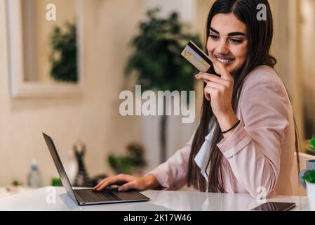 Belle jeune femme brune, en vérifiant son compte bancaire en ligne, de son bureau de compagnie. Banque D'Images