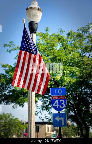 Un drapeau américain sur un poteau lumineux, se tient à côté d'un panneau de route pour l'I-43 dans Two Rivers, Wisconsin. Banque D'Images