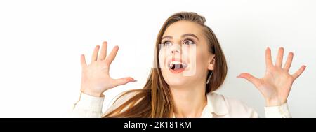 Portrait d'une jeune femme caucasienne portant une chemise blanche lève les mains et rit positivement avec la bouche ouverte regardant sur un fond blanc Banque D'Images