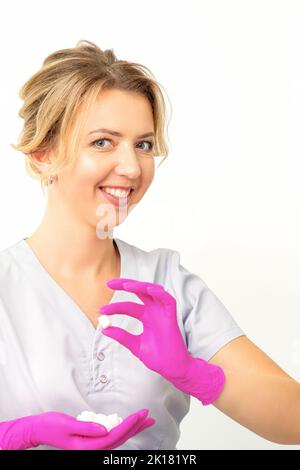 Portrait d'une jeune esthéticienne caucasienne souriante portant des gants roses tenant des cubes de sucre montrant et regardant l'appareil photo sur un fond blanc Banque D'Images