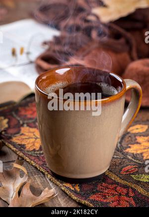 Tasse de café chaude sur tapis d'automne avec livre et couverture en arrière-plan Banque D'Images