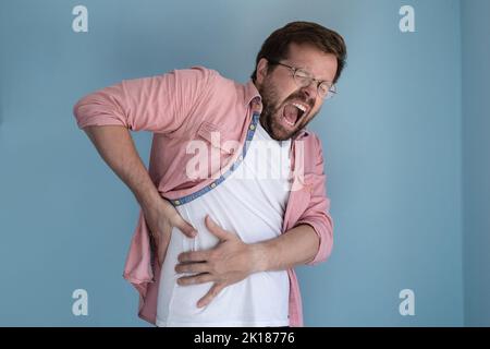 Le jeune homme éprouve de graves douleurs dans la cavité abdominale, il se tient à l'endroit douloureux avec les mains et les cris. Banque D'Images