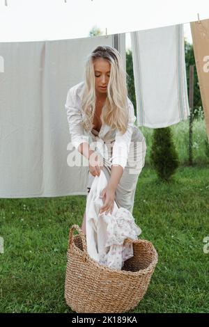 Jour de blanchisserie. Une femme porte du linge et des serviettes sur un arbre dans la cour d'une maison de village. Concept de chalet d'été. Banque D'Images