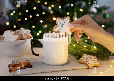 femme trempant à la main un biscuit au pain d'épice orné de flocons de neige dans une tasse à boisson chaude Banque D'Images