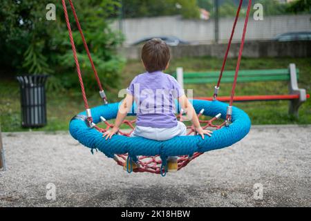 Un garçon (méconnaissable) bascule sur une balançoire en corde dans un parc pour enfants Banque D'Images